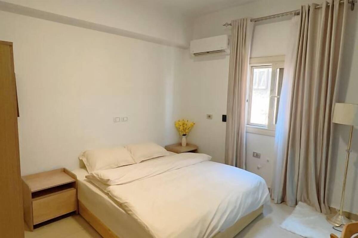 A bedroom with a bed, bedside table, lamp, and curtains.