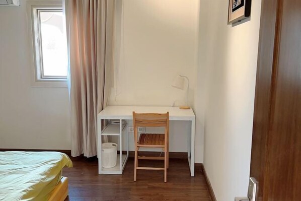 Une chambre à coucher avec un lit, un bureau avec une chaise, une fenêtre avec des rideaux et un radiateur.