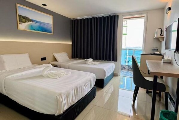 A hotel room with two beds, a desk, a chair, a TV, and a balcony with a view of the sea.