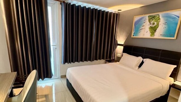 Ein Hotelzimmer mit einem großen Bett, einem Schreibtisch und einem Fenster mit Vorhängen.