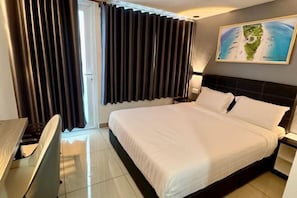 A hotel room with a large bed, a desk, and a window with curtains.