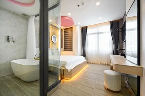 Ein modernes Badezimmer mit einer freistehenden Badewanne, einer Duschkabine aus Glas, einem Bett mit Holz-Kopfteil und einem Waschtisch mit Spiegel.
