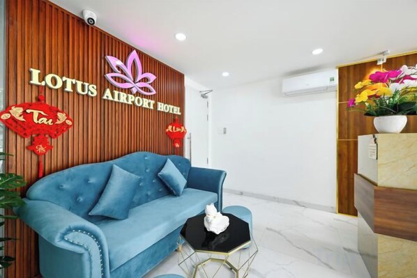 A reception area with a blue sofa, wooden paneling, and a sign for Lotus Airport Hotel.