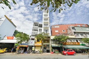 A multi-story building with various shops on the ground floor, a red car parked in front, and a clear sky.