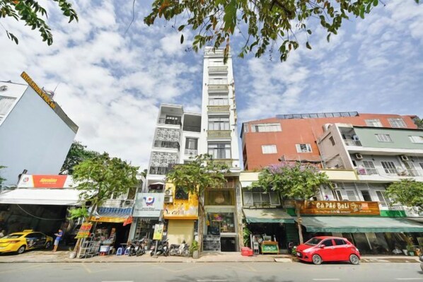 A multi-story building with various shops on the ground floor, a red car parked in front, and a clear sky.
