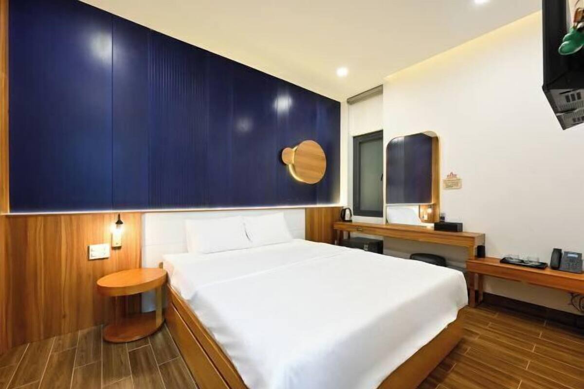 A hotel room with a large bed, a wooden nightstand, a desk with a chair, a mirror, and a television.