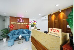 A reception area with a blue sofa, a reception desk, and a sign indicating "Lê Tân Reception". - Lotus Airport Hotel Saigon (Ho Chi Minh City)