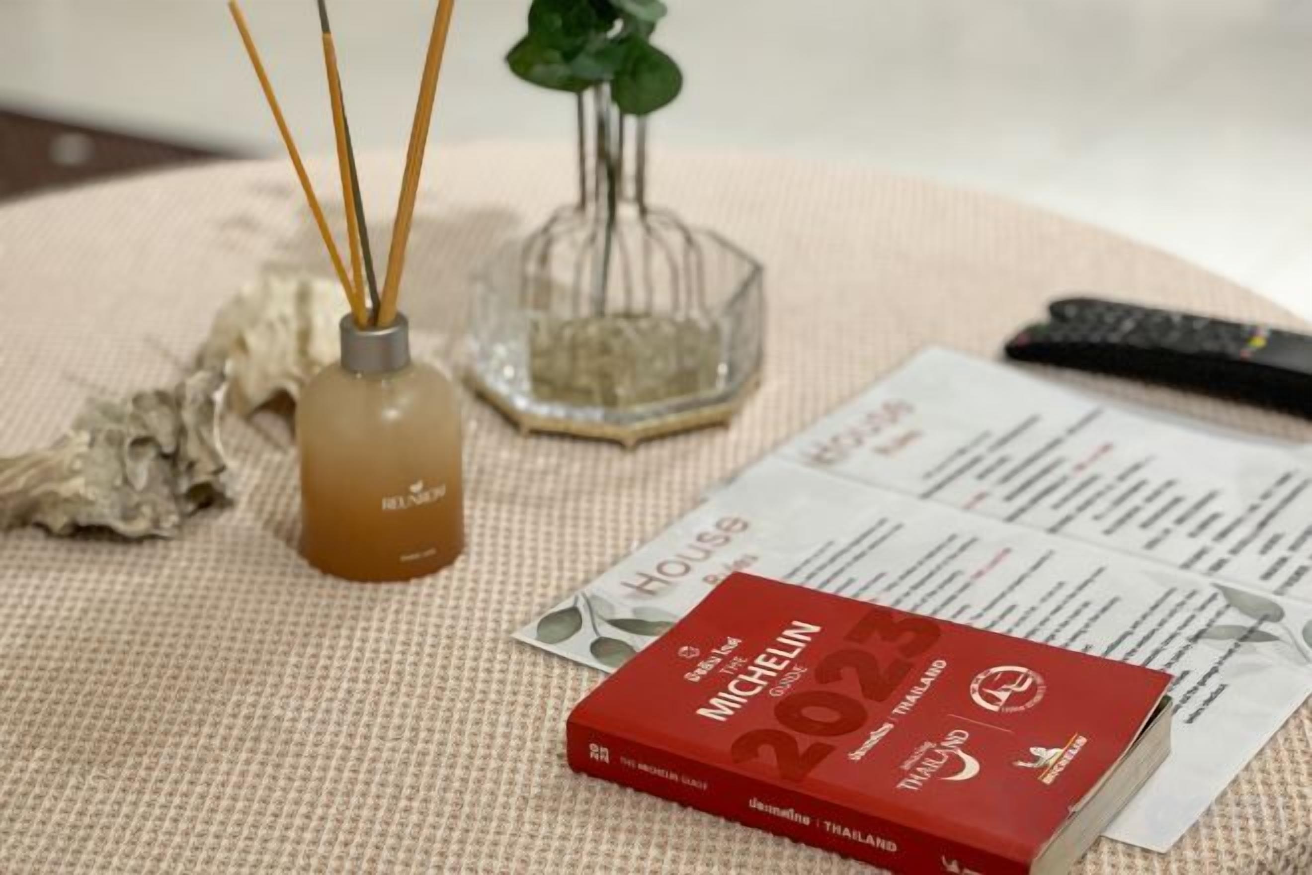 Un livre intitulé « Michelin Thaïlande 2023 » est posé sur une surface texturée, accompagné d’une télécommande et d’un objet décoratif.