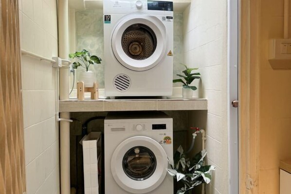 A laundry room with two stacked washing machines, a small shelf with toiletries, and a potted plant. - 3 Bedroom NORDIC HOME Full Kitchen 8 MINS to MRT & JODD Fair (Bangkok)