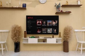 A living room with a mounted TV displaying a Netflix interface, a white sofa, and two decorative vases. - 3 Bedroom NORDIC HOME Full Kitchen 8 MINS to MRT & JODD Fair (Bangkok)