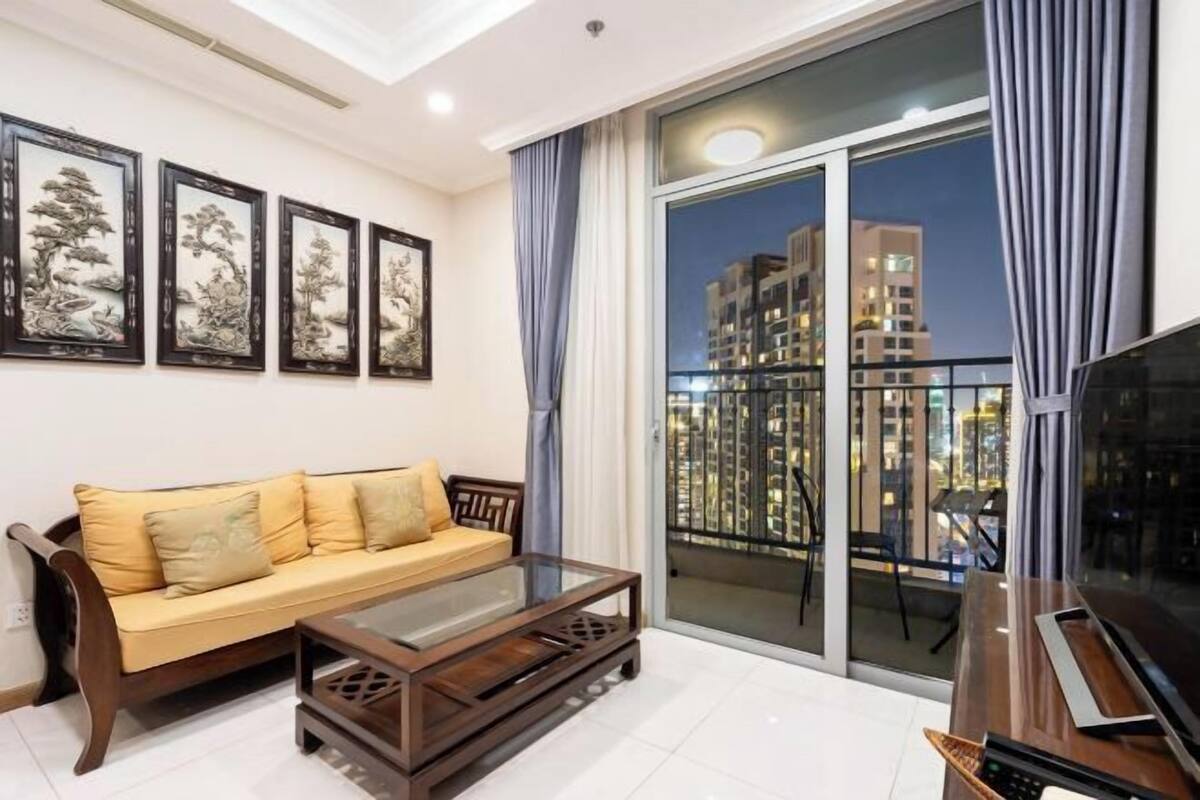 A modern living room with a sofa, coffee table, and TV, featuring artwork on the wall and a balcony with a city view.