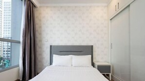 Una habitación de hotel con cama, mesita de noche, armario y ventana con cortinas.