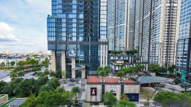 Un edificio moderno de gran altura con fachada de vidrio, rodeado de un área ajardinada con palmeras y un pavimento a cuadros.