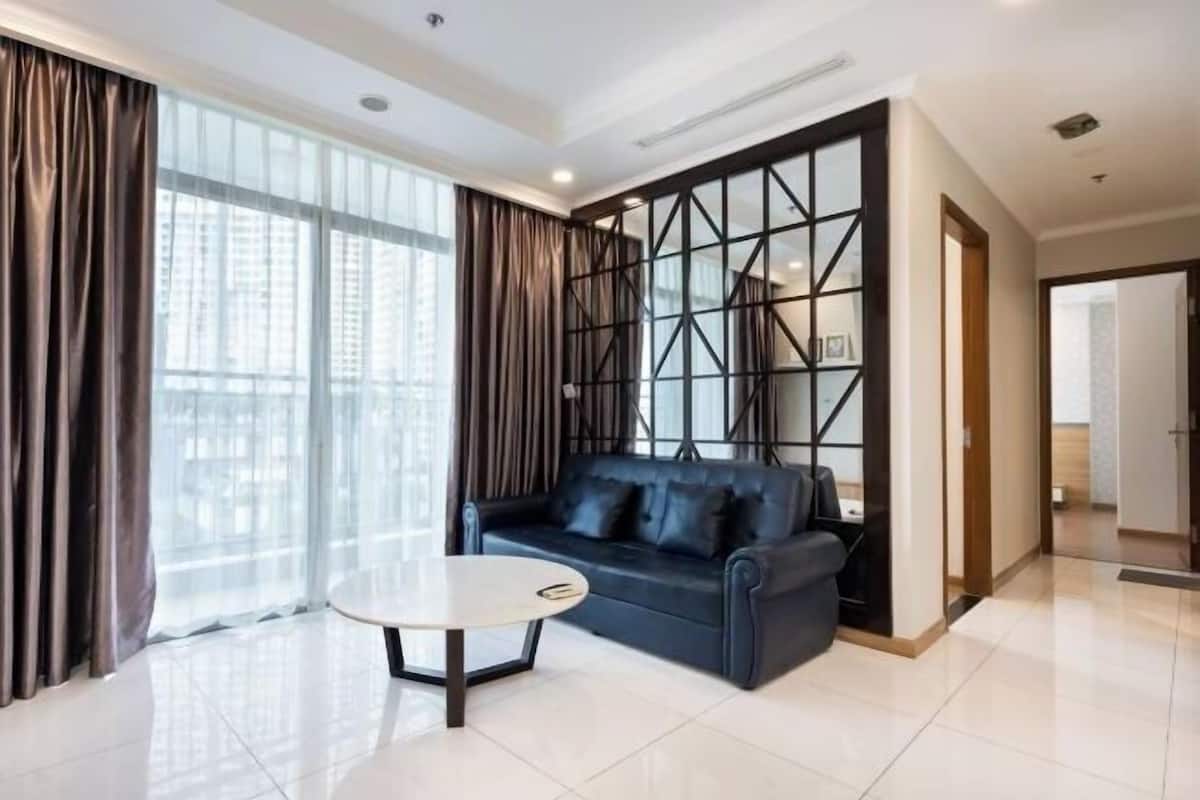 A modern living room with a black sofa, a round coffee table, and a large window with curtains.