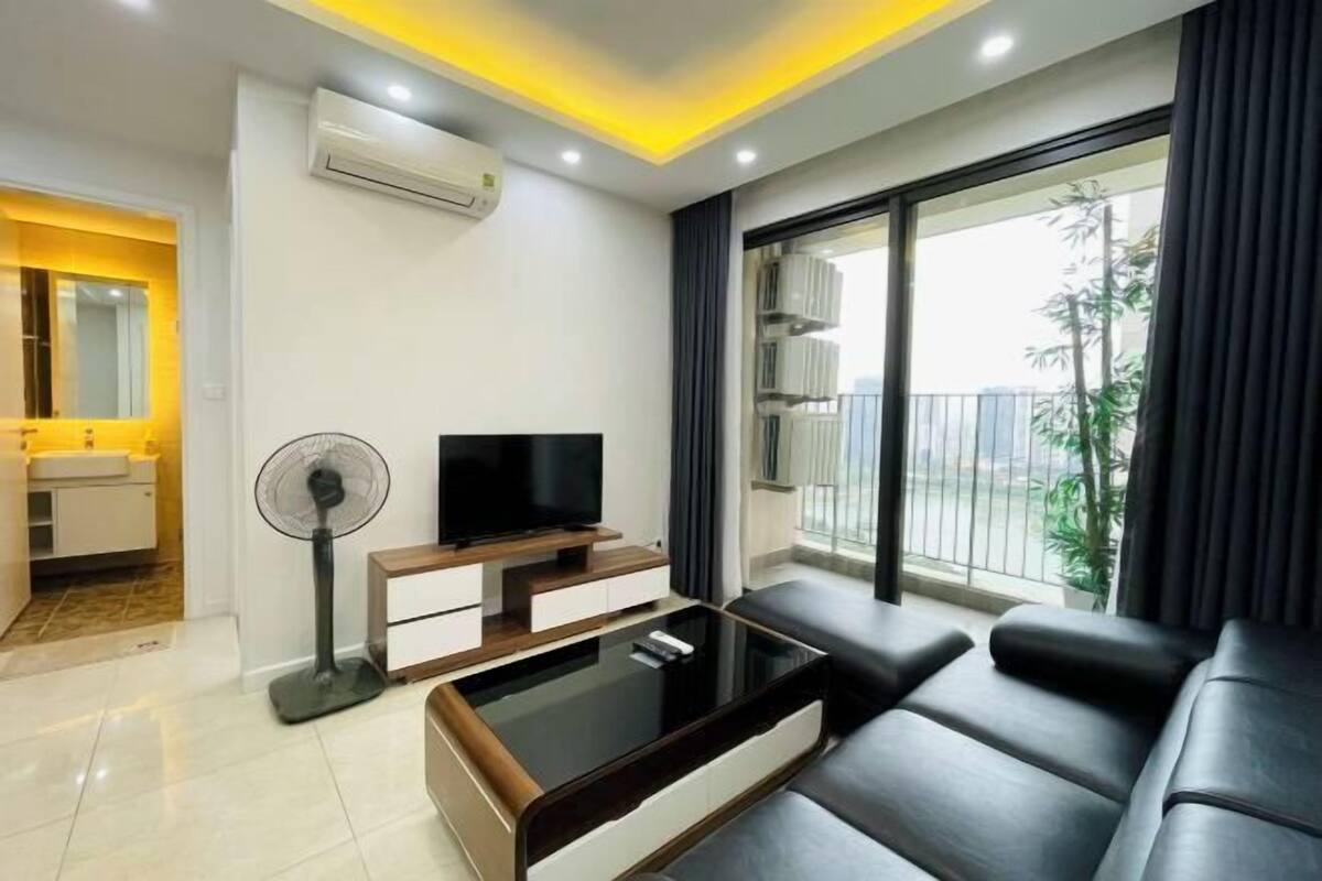 Una sala de estar moderna con un televisor de pantalla plana, una mesa de centro de vidrio, un sofá y un ventilador de pie.