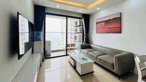 Un salon moderne avec un canapé, une table basse en verre, un téléviseur à écran plat et un tableau accroché au mur.