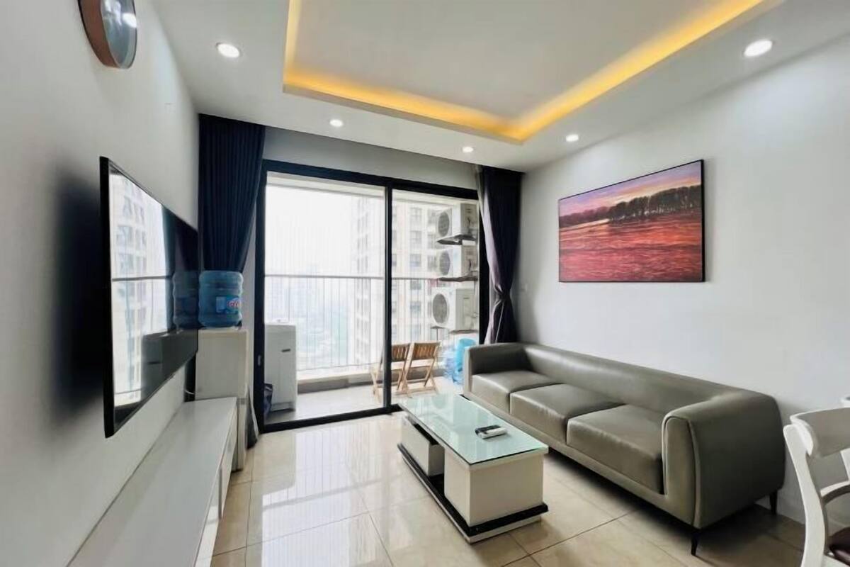 Una sala de estar moderna con un sofá, una mesa de centro de cristal, un televisor de pantalla plana y un ventanal grande.