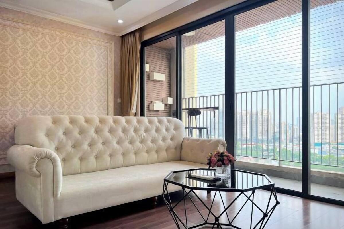 Una sala de estar con un sofá capitonado, una mesa de centro de vidrio y vistas a un paisaje urbano a través de amplios ventanales.