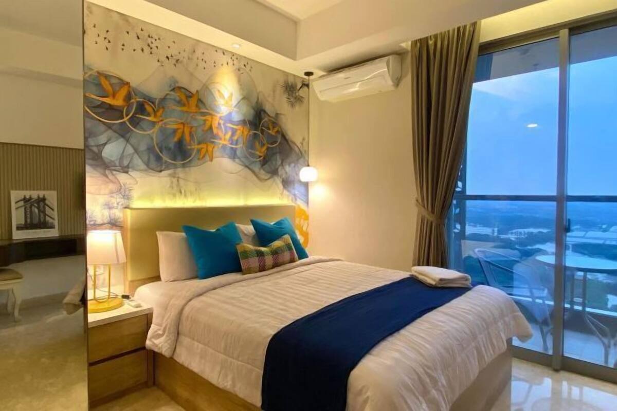 Une chambre d’hôtel avec un grand lit, une table de chevet, une œuvre d’art murale et une vue sur la ville par une grande fenêtre.