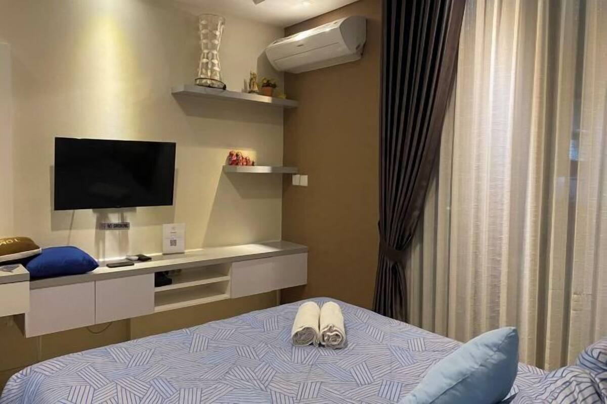 Une chambre d’hôtel équipée d’un lit, d’une télévision, d’un bureau avec un ordinateur et d’une fenêtre avec des rideaux.