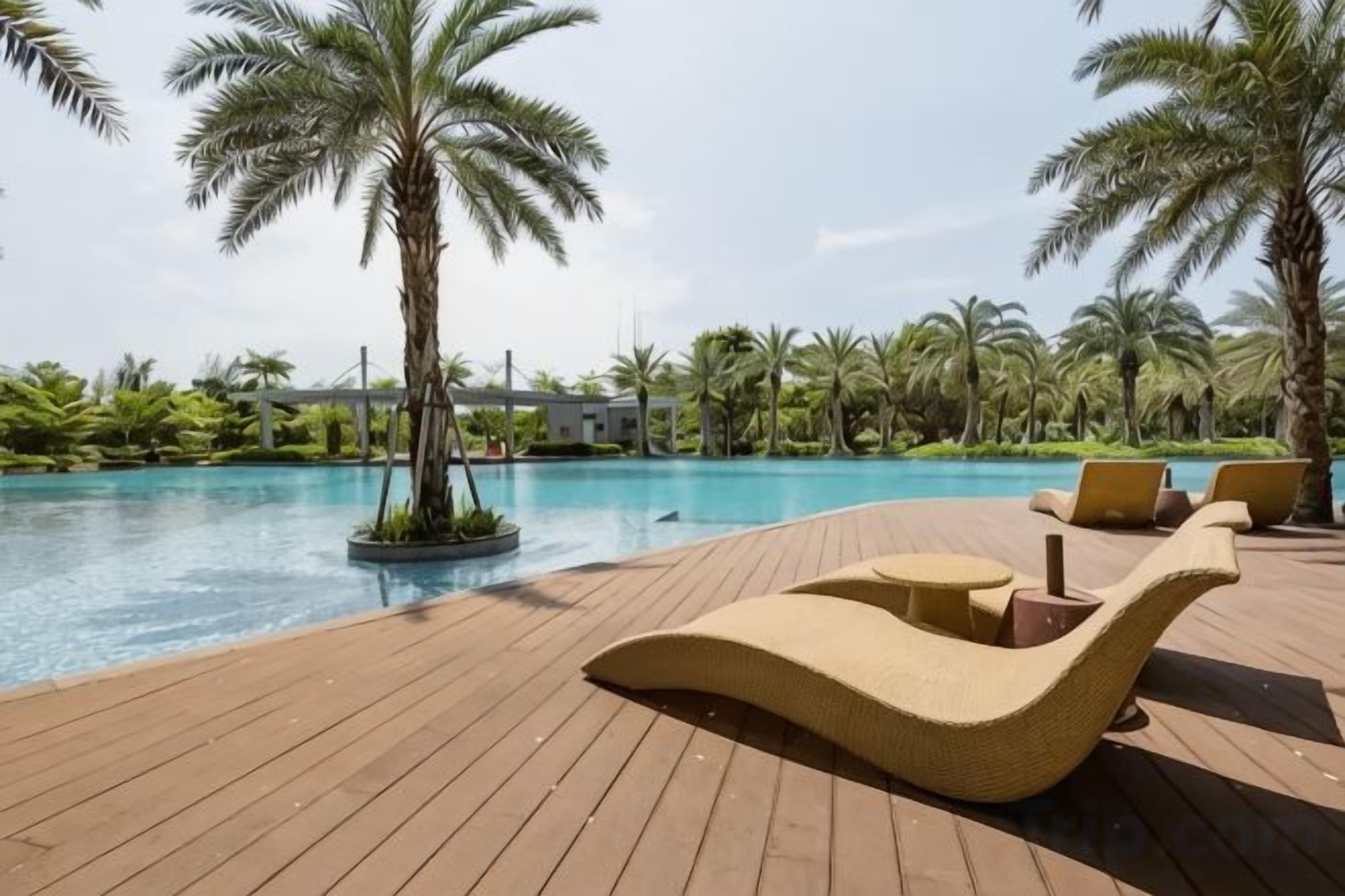 A wooden deck with lounge chairs and a pool, surrounded by palm trees.