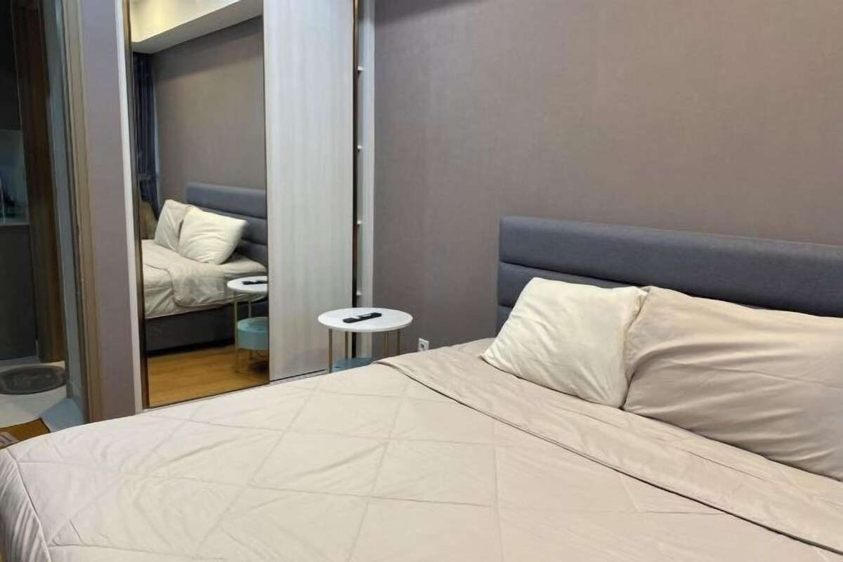 Une chambre à coucher comprenant un lit, une table de chevet, un miroir et donnant sur une pièce adjacente.