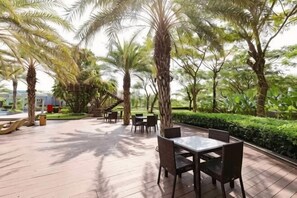 An outdoor patio with tables and chairs, surrounded by palm trees and greenery.