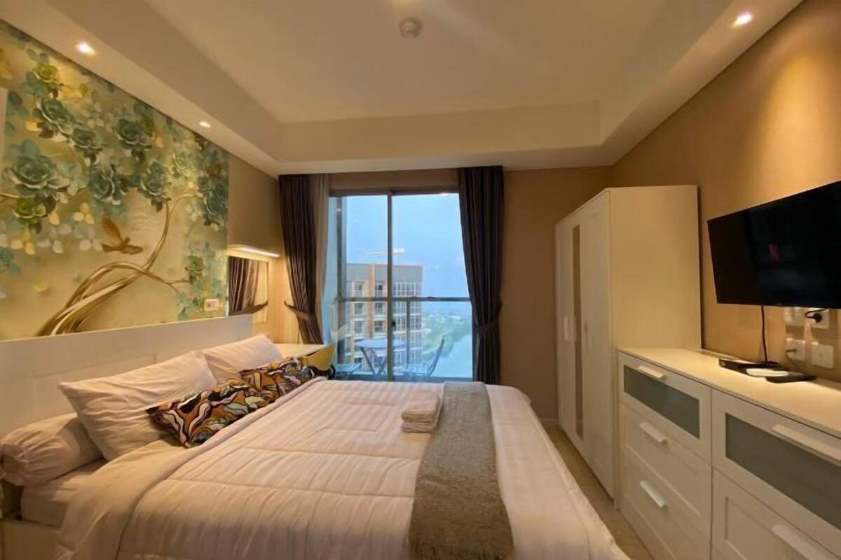 Une chambre d’hôtel équipée d’un lit, d’une télévision, d’une armoire et d’un balcon avec vue sur les bâtiments.