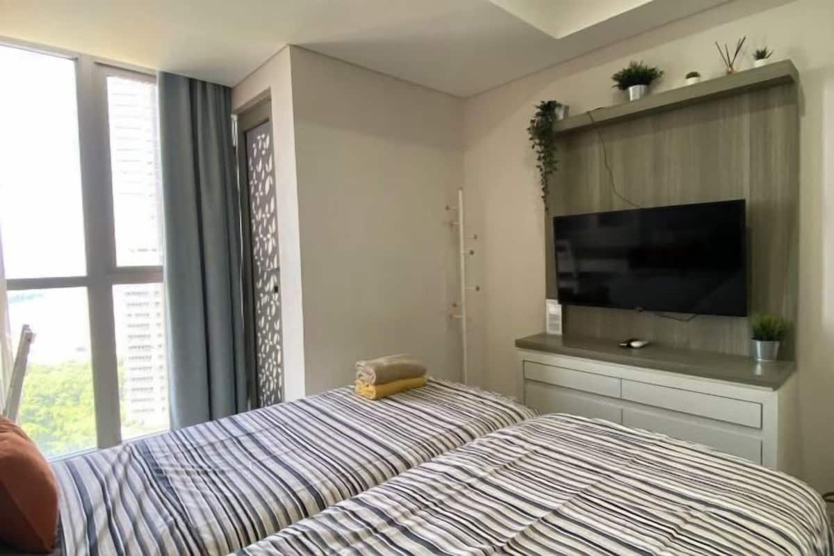 Une chambre avec deux lits, un téléviseur posé sur un meuble en bois et une fenêtre avec des rideaux.