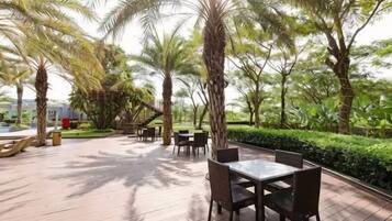 An outdoor patio with tables and chairs, surrounded by palm trees and greenery.