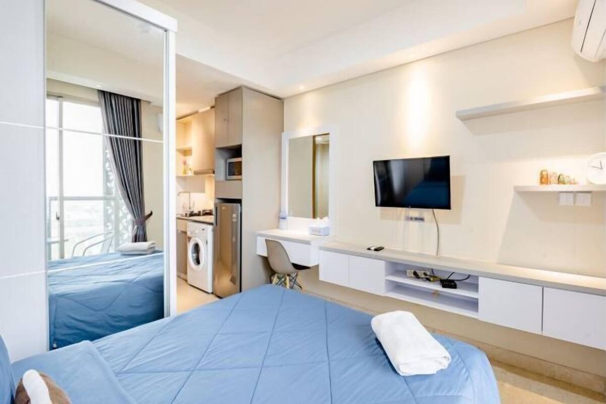 Une chambre d’hôtel équipée d’un lit, d’un bureau, d’une télévision, d’une machine à laver et d’une fenêtre avec des rideaux.