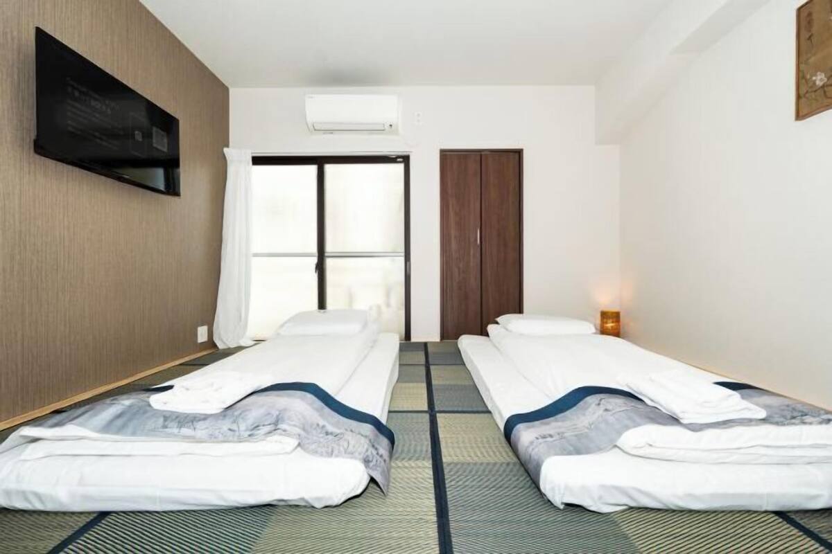Ein Hotelzimmer mit zwei Einzelbetten, einer Schiebetür, einem an der Wand befestigten Fernseher und einem kleinen Nachttisch mit Lampe.