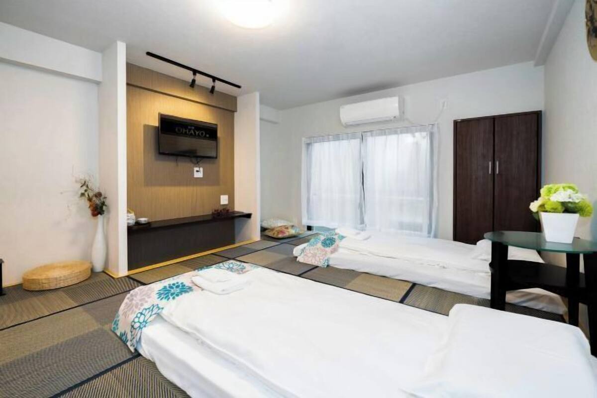 Ein Hotelzimmer mit zwei Betten, einem Fernseher, einem Kleiderschrank und einem kleinen Tisch mit einer Vase.