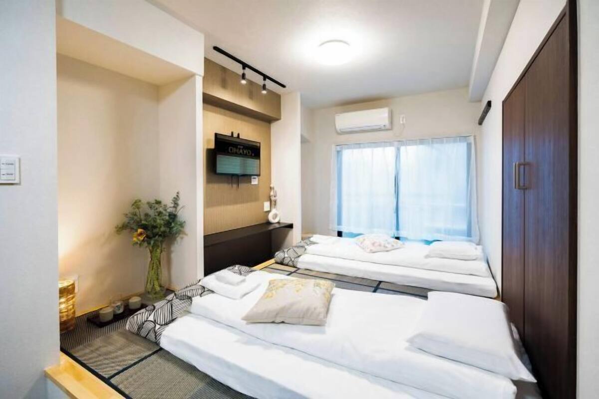 Ein Hotelzimmer mit zwei Betten, einem Fernseher, einem Fenster mit Vorhängen und einem Holzschrank.