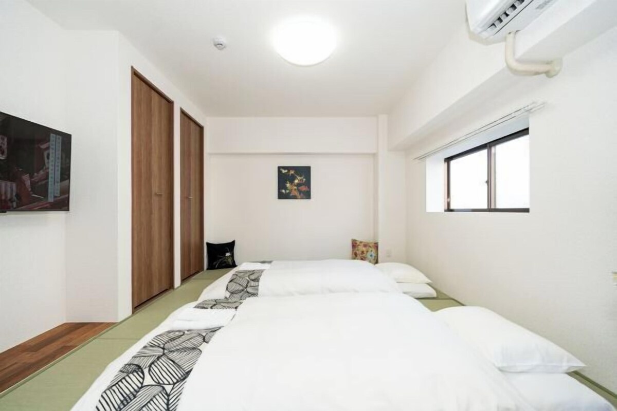 A hotel room with two beds, a window, a ceiling light, and a wall-mounted air conditioner.