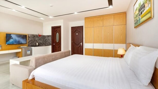 A modern hotel room with a large bed, a desk with a TV, a wardrobe, and a painting on the wall. - PINE TREE APT (Ho Chi Minh City)