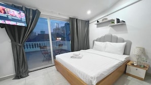 A modern hotel room with a large bed, a TV on the wall, a balcony with a city view, and a small table with a lamp. - PINE TREE APT (Ho Chi Minh City)