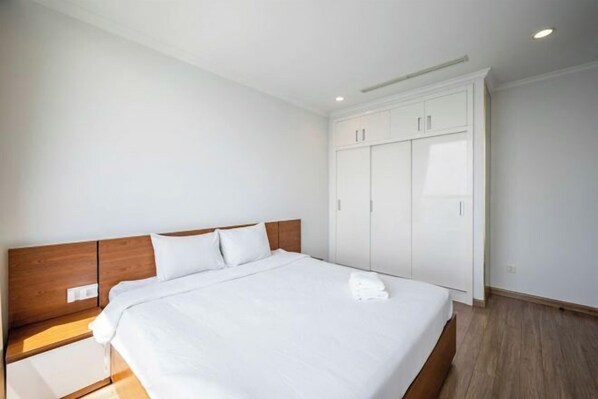 Une chambre d’hôtel avec un grand lit, une tête de lit en bois, du linge de lit blanc, une armoire et une table de chevet.