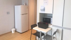 Et kompakt køkken med køleskab, mikroovn og et lille bord med stole.
