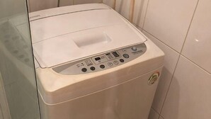 En hvid vaskemaskine med kontrolpanel, placeret i et badeværelse med fliserede vægge.