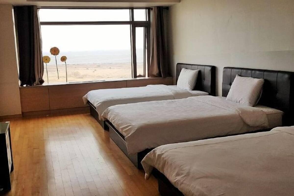 A hotel room with two beds, a large window with a view of the beach, and a wooden floor.