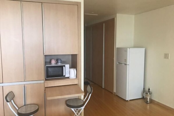 A compact kitchen with a microwave, kettle, and a refrigerator. There is a small table with two chairs.