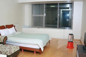 Een slaapkamer met een bed, een raam met jaloezieën, een nachtkastje en een rood apparaat.