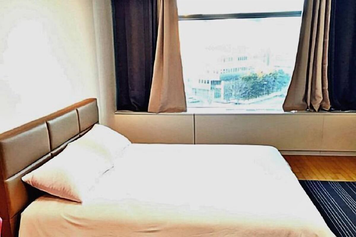 A hotel room with a bed, a window with curtains, and a view of buildings outside.