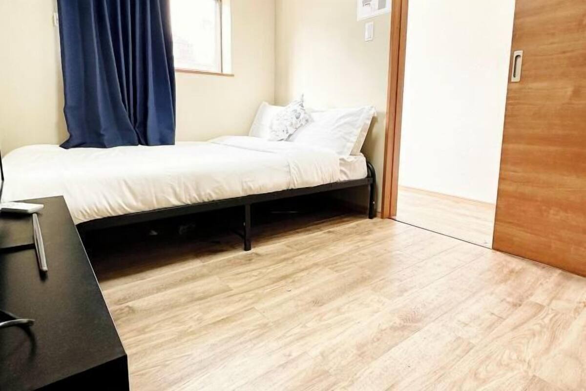 A single bed with white bedding, a wooden floor, a desk with a chair, and a blue curtain.
