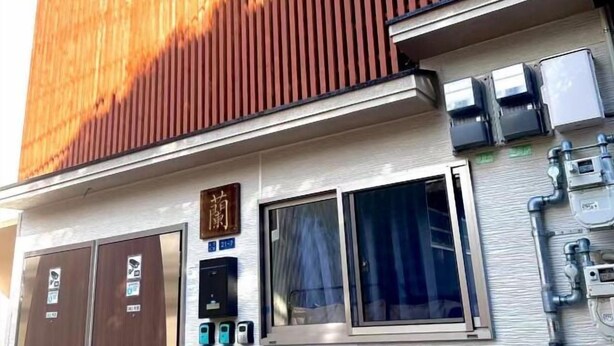 Fachada de hotel de madera, con un cartel y una ventana con cortinas.