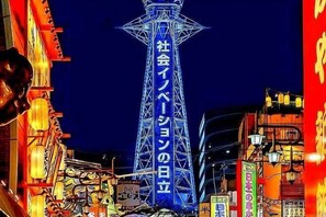 Ein hell erleuchteter Turm mit japanischem Text, umgeben von Gebäuden mit beleuchteten Schildern.
