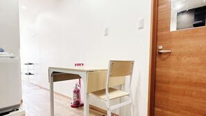 Una habitación pequeña con una puerta de madera, una mesa blanca con una silla y un electrodoméstico blanco en la esquina.