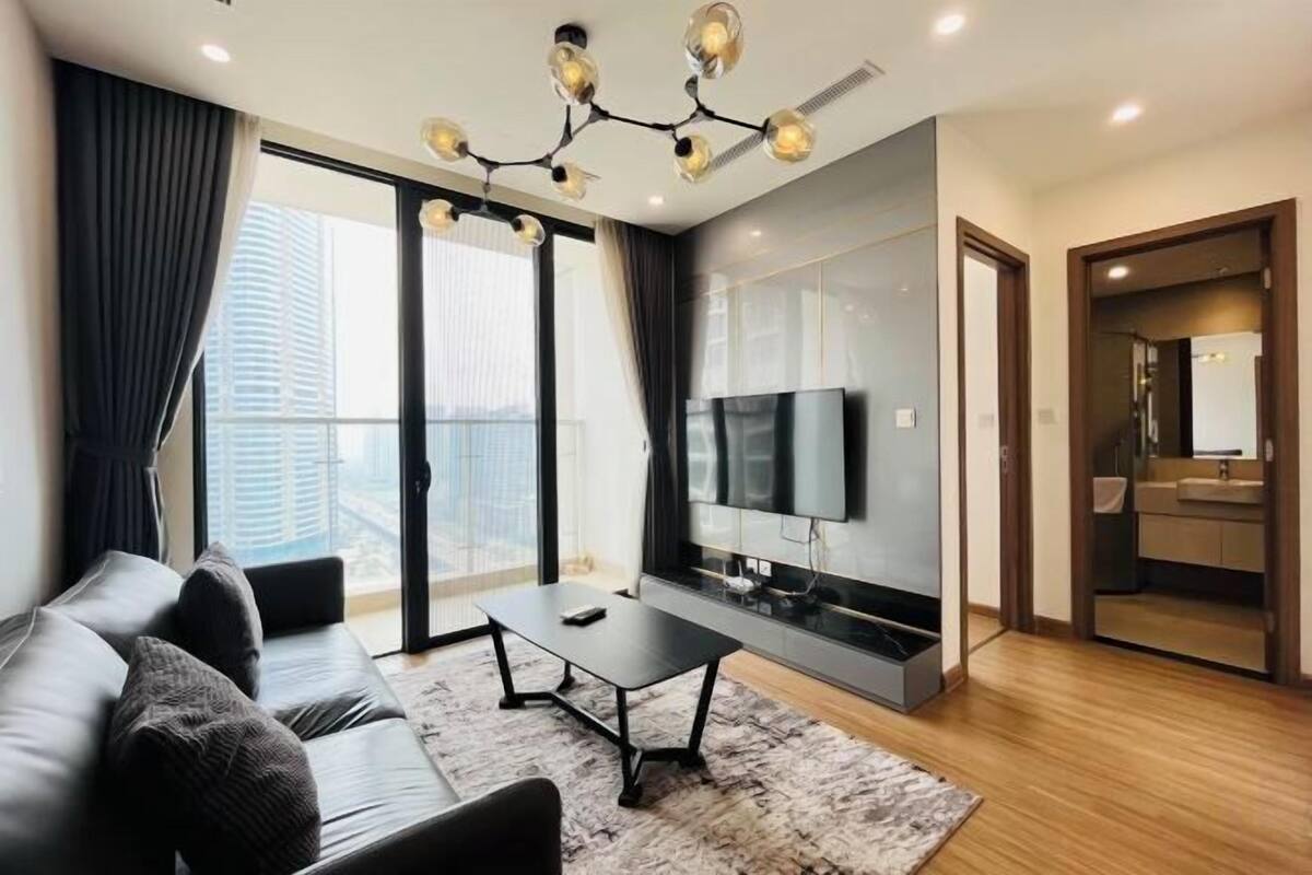 Uma sala de estar moderna com sofá, mesa de centro, TV e uma grande janela com cortinas.