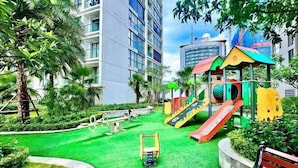 A playground with slides and swings, surrounded by greenery and a building in the background. - Sophia Housing - Vinhomes Sky Lake Pham Hung (Hanoi)